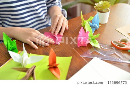 Female hands folding paper birds colorful as a hobby on a wooden table at home 133696773