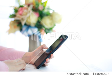 Hands of woman in pink shirt holding smart phone on white table top 133696828