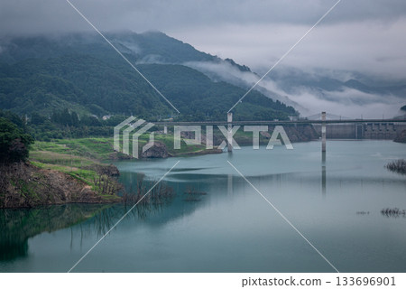A tranquil early morning view of the Yamba Dam Lake and misty mountains (Gunma Prefecture) 133696901