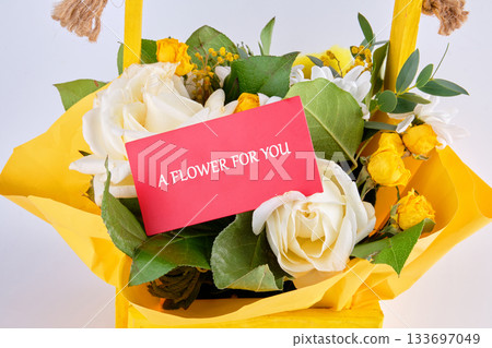 A beautiful display of yellow roses and white flowers is nestled in a cheerful yellow basket. A note tucked among the blooms expresses affection and happiness for the recipient 133697049