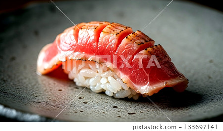 Wabi-sabi aesthetic. a single piece of nigiri with seared otoro, focusing on the marbled fat melting over the rice, on a rough-textured ceramic plate with visible craft marks  133697141