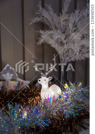 Glowing decorative reindeer surrounded by shimmering tinsel and winter branches indoors Glowing decorative reindeer surrounded by shimmering tinsel and winter branches indoors 133698503