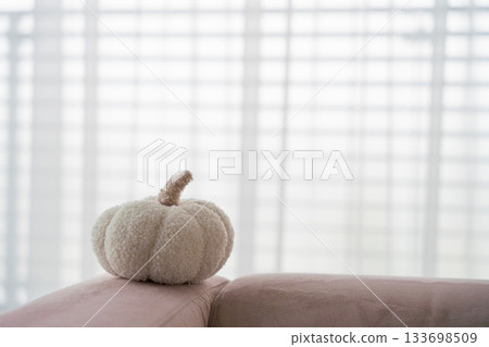 Cozy white fabric pumpkin on pastel sofa with soft light and blurred window blinds background Cozy white fabric pumpkin on pastel sofa with soft light and blurred window blinds background 133698509