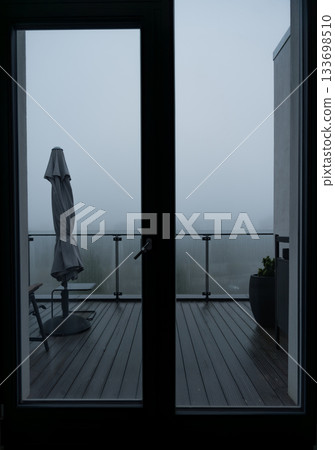 Autumn foggy morning view of balcony with closed umbrella seen through glass door in modern home Autumn foggy morning view of balcony with closed umbrella seen through glass door in modern home 133698510