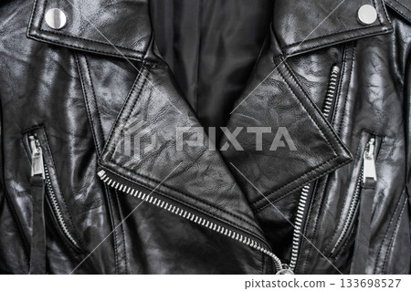 Close-up of shiny black faux leather biker jacket with silver zippers and snap button collar. Close-up of shiny black faux leather biker jacket with silver zippers and snap button collar. 133698527