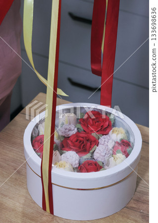 Female entrepreneur assembling marshmallow flowers in a hat box for a gift, tying it with colorful ribbons, marshmallow tulips and roses. 133698636