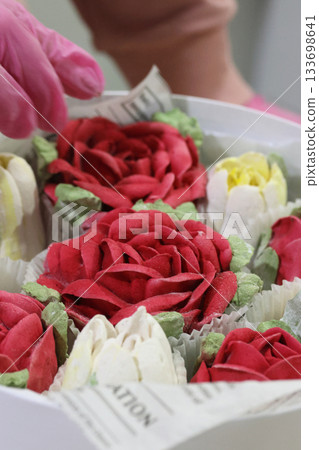 Female entrepreneur assembling marshmallow flowers in a hat box, marshmallow tulips and roses, homemade marshmallow. Oblique Angle. Close-up. Female entrepreneur assembling marshmallow flowers in a hat box, marshmallow tulips and roses, homemade marshmallow. Oblique Angle. Close-up. 133698641
