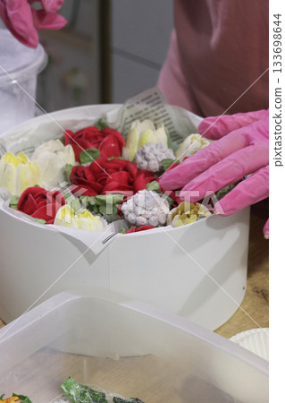 Female entrepreneur assembling marshmallow flowers in a hat box, marshmallow tulips and roses, homemade marshmallow. Oblique Angle. 133698644