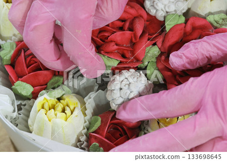 Female entrepreneur assembling marshmallow flowers in a hat box, marshmallow tulips and roses, homemade marshmallow. Close-up. 133698645