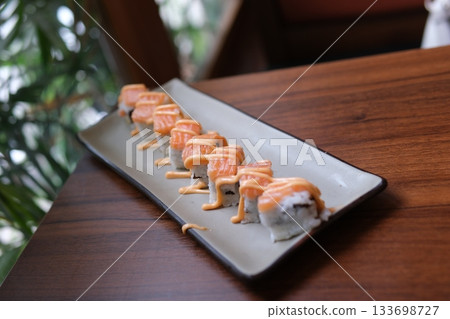 Elegant platter featuring fresh salmon nigiri arranged with artisanal sushi rolls including grilled eel drizzled with sauce, vibrant tuna and salmon cubes, mango topped rolls. Elegant platter featuring fresh salmon nigiri arranged with artisanal sushi rolls including grilled eel drizzled with sauce, vibrant tuna and salmon cubes, mango topped rolls. 133698727