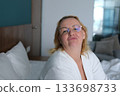 Home, kiss and portrait of woman on bed for relaxing, resting and comfortable in bedroom in morning. Apartment, blanket and person with wink, pout and wake up for health, wellness and weekend 133698733