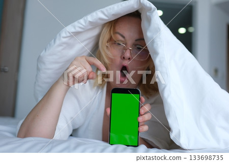 green screen for chroma key advertising Shocked lady staring at smartphone with open mouth. Middle-aged woman reading surprising message on phone, amazing news at night 133698735