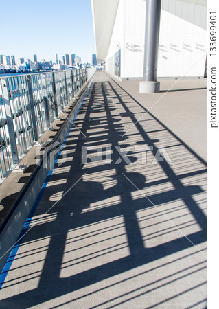 The shadow of a fence with alphabet letters reflected on the pier deck and the Tokyo skyscrapers in the distance, Odaiba, Tokyo 133699401