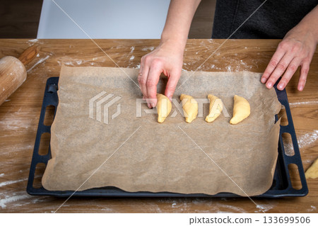 Arranging Unbaked Pastries on Large Parchment-Lined Baking Tray in Kitchen 133699506