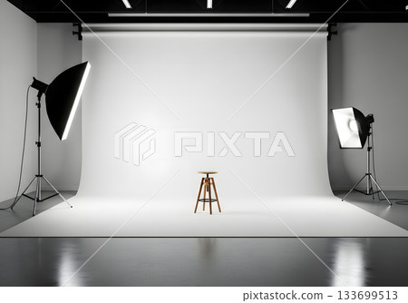 Professional photography studio with an empty white cyclorama background. Lighting equipment and a single stool on set for a photoshoot. Minimalist production concept with copy space 133699513
