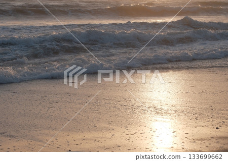 Shoreline at the beach with a setting sun, waves sand and no people 133699662