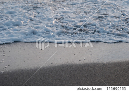 Shoreline at the beach with a setting sun, waves sand and no people 133699663