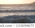 Shoreline at the beach with a setting sun, waves sand and no people 133699675