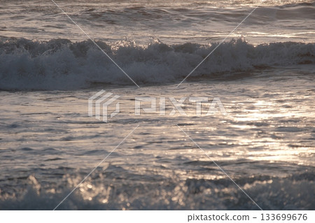 Shoreline at the beach with a setting sun, waves sand and no people 133699676