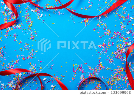 Red ribbon loops and confetti decorate a bright blue festive surface. Happy New Year and Christmas designs. With space for text. Red ribbon loops and confetti decorate a bright blue festive surface. Happy New Year and Christmas designs. With space for text. 133699968