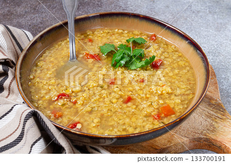 Warm lentil soup with vegetables garnished with fresh cilantro served in a rustic bowl on a textured surface 133700191