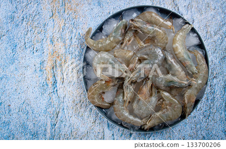 Fresh raw shrimp spread on ice with lemon and cilantro slices on a marble surface, ready to cook, no people 133700206