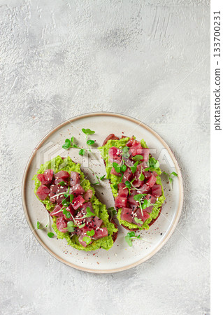 toasts with fresh tuna and avocado, spread on black bread and sprinkled with microgreens, breakfast, healthy food 133700231