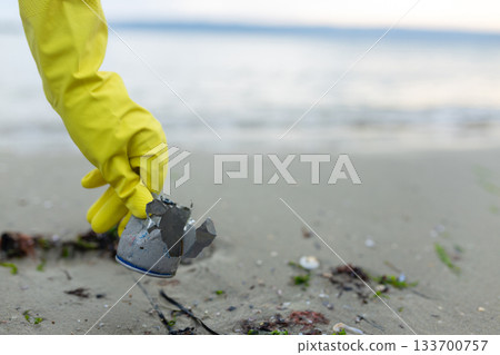volunteer picking up a crushed metal can during beach cleanup, highlighting pollution, waste problem, ecology, coastal protection and environmental awareness. volunteer picking up a crushed metal can during beach cleanup, highlighting pollution, waste problem, ecology, coastal protection and environmental awareness. 133700757