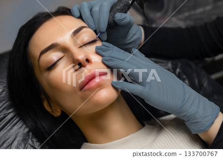 Close up of a cosmetologist performing eyelid permanent makeup, precision eyeliner tattoo procedure with sterile tools, enhancing lash line and eye beauty in a professional studio. Close up of a cosmetologist performing eyelid permanent makeup, precision eyeliner tattoo procedure with sterile tools, enhancing lash line and eye beauty in a professional studio. 133700767
