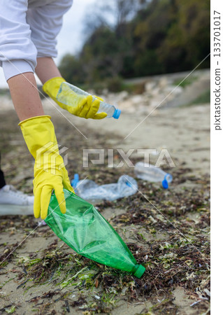 volunteer collecting plastic bottles on a polluted beach, highlighting ocean pollution, waste problem, environmental protection and coastal cleanup action. volunteer collecting plastic bottles on a polluted beach, highlighting ocean pollution, waste problem, environmental protection and coastal cleanup action. 133701017