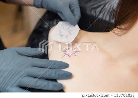 tattoo artist applying a stencil of a sun design onto a client chest, preparing the placement before starting the tattoo session. tattoo artist applying a stencil of a sun design onto a client chest, preparing the placement before starting the tattoo session. 133701022