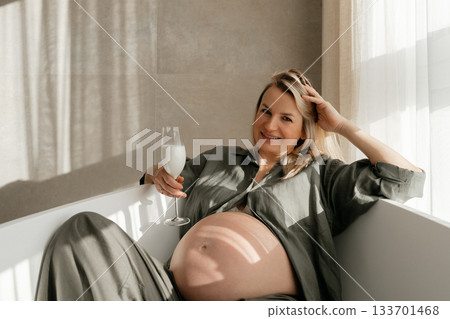 34 week, A serene maternity portrait of a pregnant woman relaxing in a bathtub with soft daylight illuminating her silhouette. The calm atmosphere, gentle shadows and natural setting create a warm 133701468