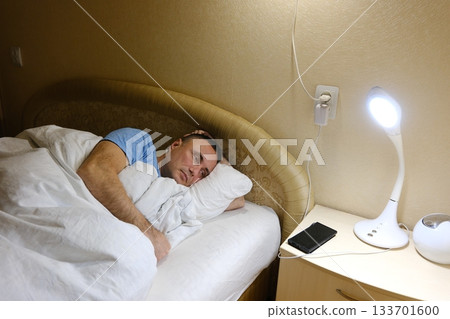 man lies in bed at night, smartphone screen, deep in thought. dim lighting and focused expression. Themes of insomnia, social media addiction, stress, late-night scrolling 133701600