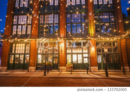 Historic brick building decorated with warm string lights in the Distillery District of Toronto during the evening. 133702005
