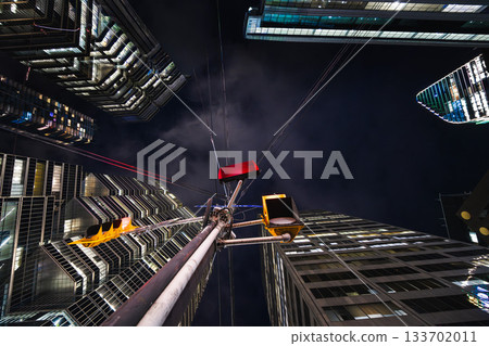 A lone traffic signal rises into a canyon of towering glass, its red glow contrasting with the cold geometry of the surrounding skyscrapers. 133702011