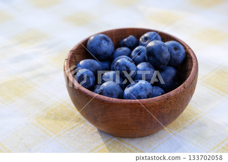 A rustic wooden bowl, filled with fresh blueberries, sits on a delicate tablecloth. A great fit for promotions related to health and dieting. Copy space A rustic wooden bowl, filled with fresh blueberries, sits on a delicate tablecloth. A great fit for promotions related to health and dieting. Copy space 133702058