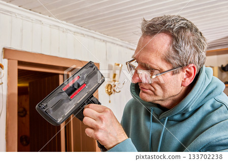 Cleaning rollers of vacuum cleaner head from hair wound on axle, man over fifty concentrated removes debris. Cleaning rollers of vacuum cleaner head from hair wound on axle, man over fifty concentrated removes debris. 133702238