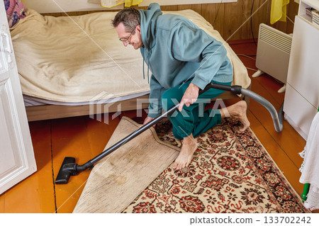 Mature man uses vacuum cleaner to clean country house. Mature man uses vacuum cleaner to clean country house. 133702242