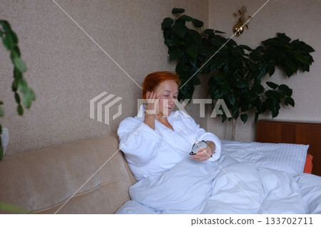 Middle age woman is waking up, stretching arms at bedroom. Eye rubbing after waking up in bed Middle age woman is waking up, stretching arms at bedroom. Eye rubbing after waking up in bed 133702711