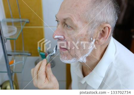 Portrait of an elderly senior man, face, shaving cream on beard, skincare treatment in front of mirror in bathroom. Healthy active mature man morning shave routine, vitality, hygiene, domestic life Portrait of an elderly senior man, face, shaving cream on beard, skincare treatment in front of mirror in bathroom. Healthy active mature man morning shave routine, vitality, hygiene, domestic life 133702734
