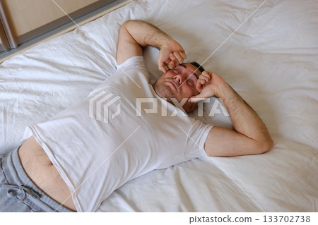 Mid adult man stretching while waking up in the morning in bedroom. Copy space.  133702738
