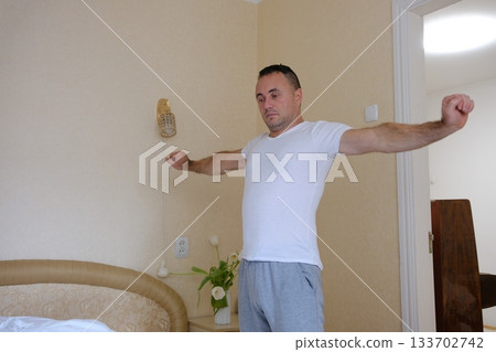 Active Young Man Stretching His Muscles Outdoors Wearing Sporty Attire While Preparing For His Workout Routine Near A Marina Surrounded By Boats And Yachts In The Bright Morning Sunlight 133702742