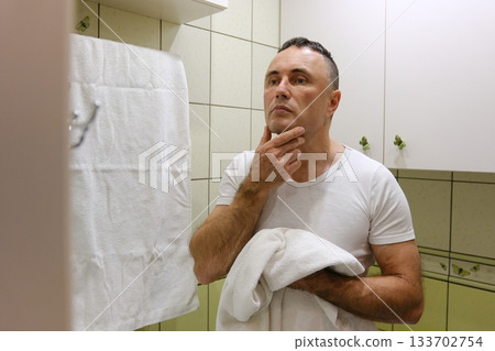 A man shaves his face in a bathroom with butterflies on the wall and light green tiles. white man shaving with brush and shaving foam looking in the mirror A man shaves his face in a bathroom with butterflies on the wall and light green tiles. white man shaving with brush and shaving foam looking in the mirror 133702754