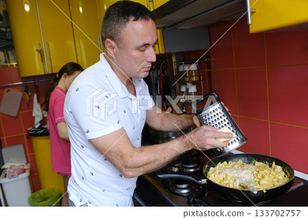 Father and daughter cooking pasta in the kitchen. Family values: dining together at home with family. Yellow kitchen. Modern interior. 133702757
