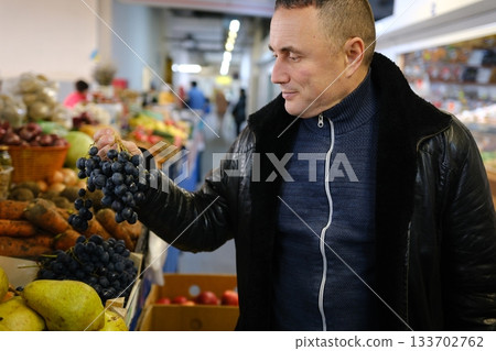 Closed up hand holding grapes, Black grapes background, Bunches of black grapes at a market, branch of black ripe grapes in men hand Closed up hand holding grapes, Black grapes background, Bunches of black grapes at a market, branch of black ripe grapes in men hand 133702762