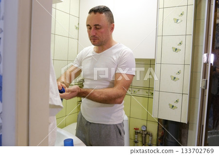 A man shaves his face in a bathroom with butterflies on the wall and light green tiles. white man shaving with brush and shaving foam looking in the mirror 133702769