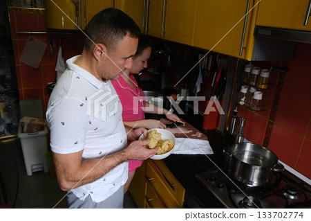 Father and daughter cooking pasta in the kitchen. Family values: dining together at home with family. Yellow kitchen. Modern interior. 133702774