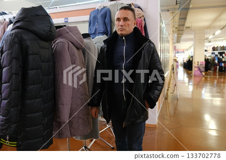 An adult man walks past women's jackets in a store 133702778