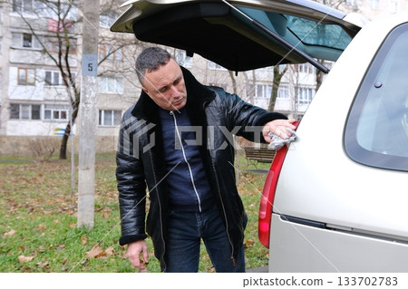 The man looks after the car from all sides, opens the doors and gets into it. man polishes a black car with a polisher The man looks after the car from all sides, opens the doors and gets into it. man polishes a black car with a polisher 133702783