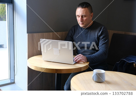 Handsome mature man sitting on sofa uses laptop while working at home. Remote working concept. Surf internet. Handsome mature man sitting on sofa uses laptop while working at home. Remote working concept. Surf internet. 133702788